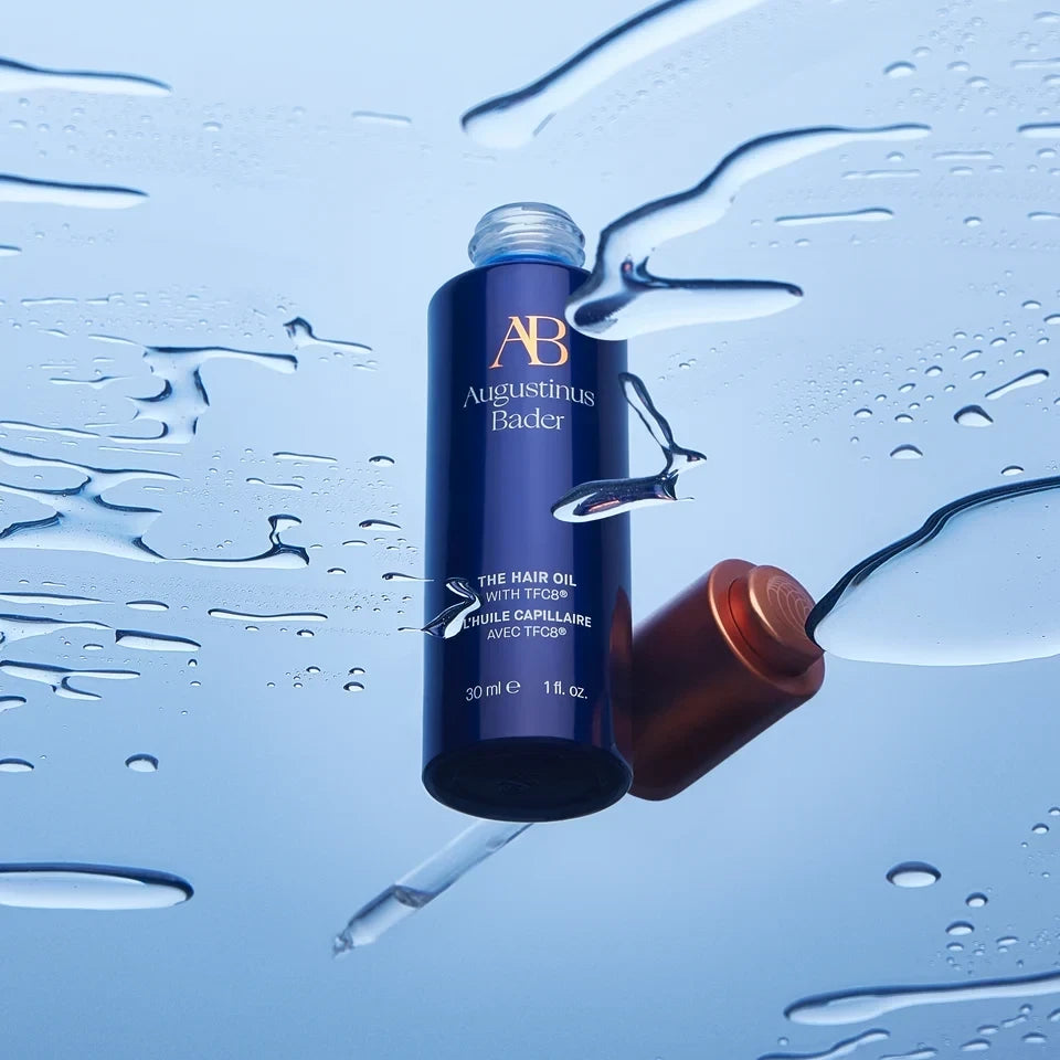 Shop Rescue Spa Augustinus Bader The Hair Oil in a blue bottle with a copper cap surrounded by water droplets