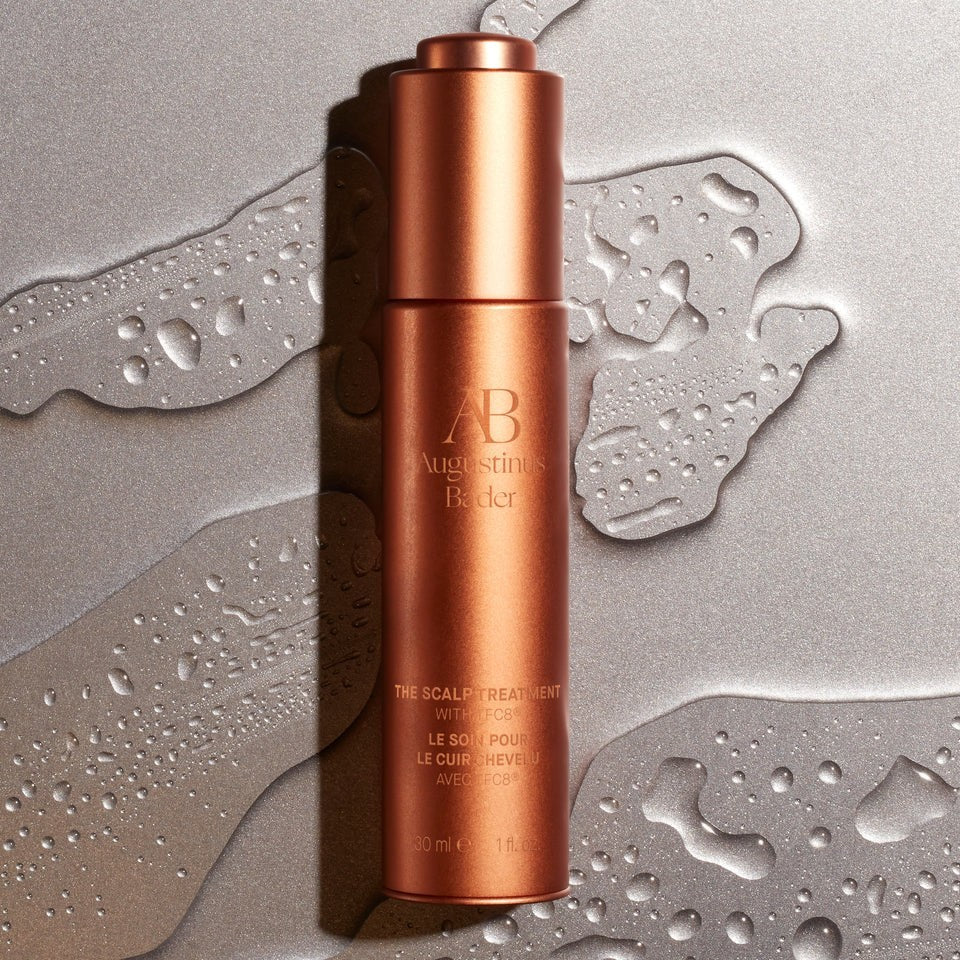 Shop Rescue Spa Augustinus Bader The Scalp Treatment serum in a metallic copper bottle on a wet, reflective surface.