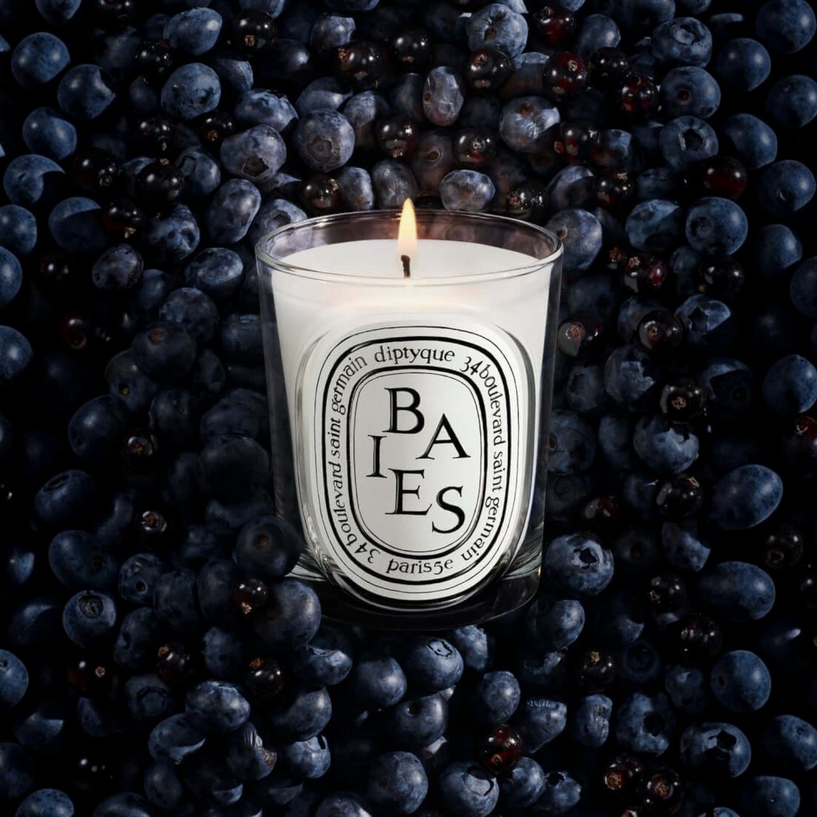 Shop Rescue Spa Baies candle in a glass vessel surrounded by a bed of fresh dark blackcurrants and blueberries