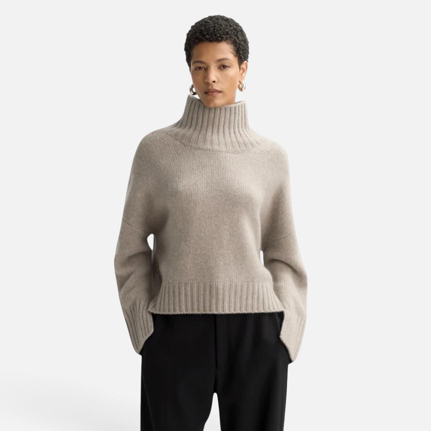 Model wearing a Shop Rescue Spa beige chunky cashmere turtleneck sweater with sleeve slits and a relaxed fit.
