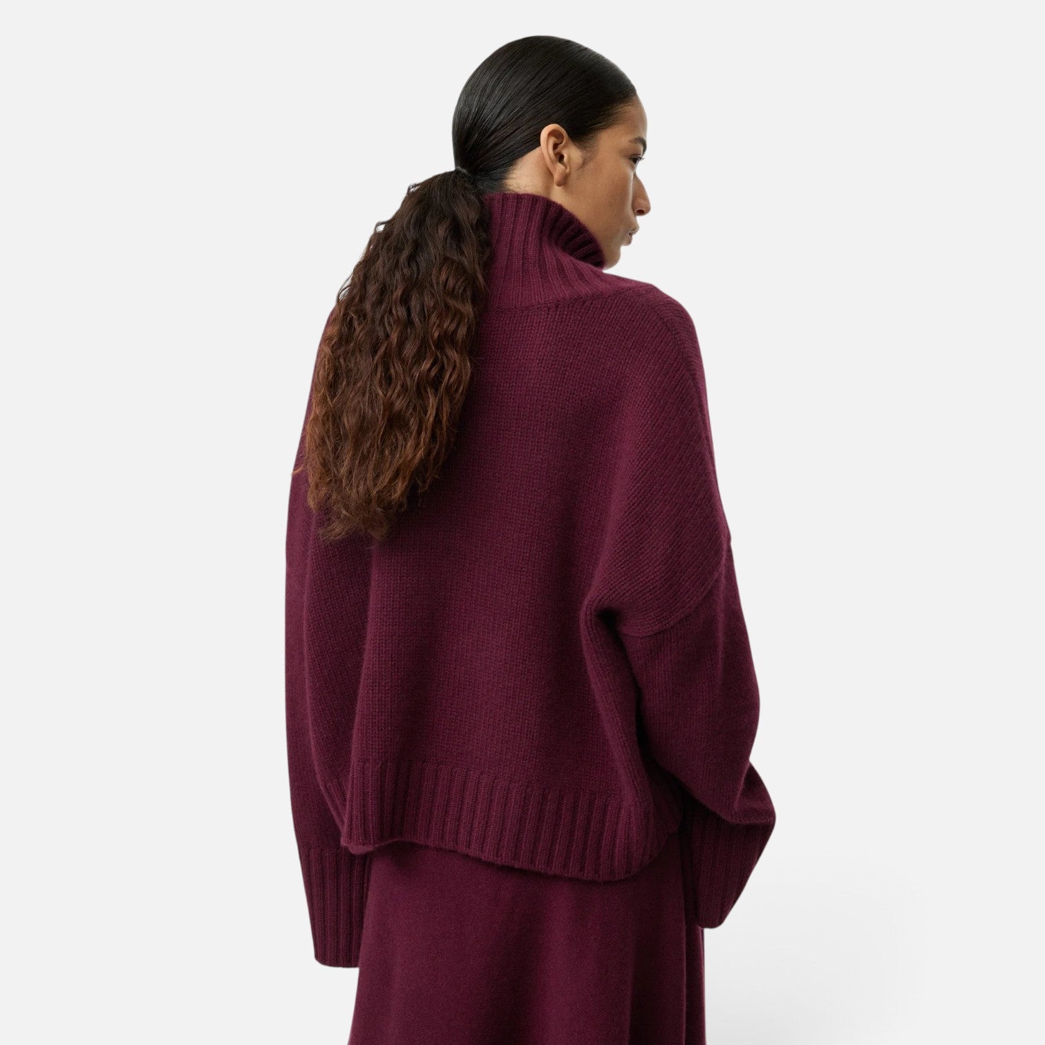 Shop Rescue Spa burgundy chunky knit cashmere turtleneck sweater with sleeve slits worn by a model from behind