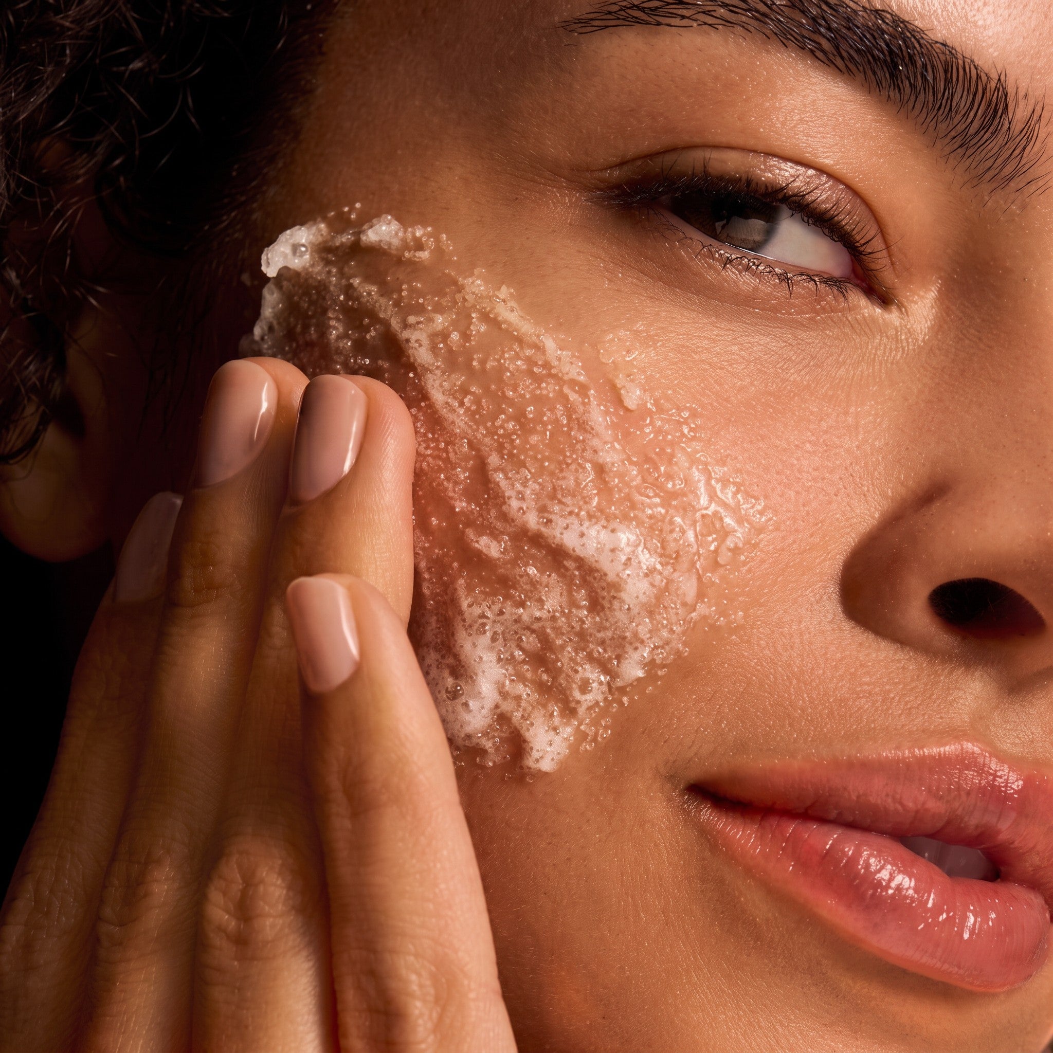 Shop Rescue Spa model applying IS Clinical Cleansing Complex Polish, a textured exfoliating scrub on her cheek.