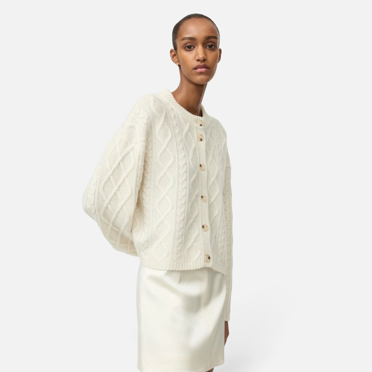 Shop Rescue Spa cream cable knit cashmere cardigan with button front, worn by a model against a neutral background.