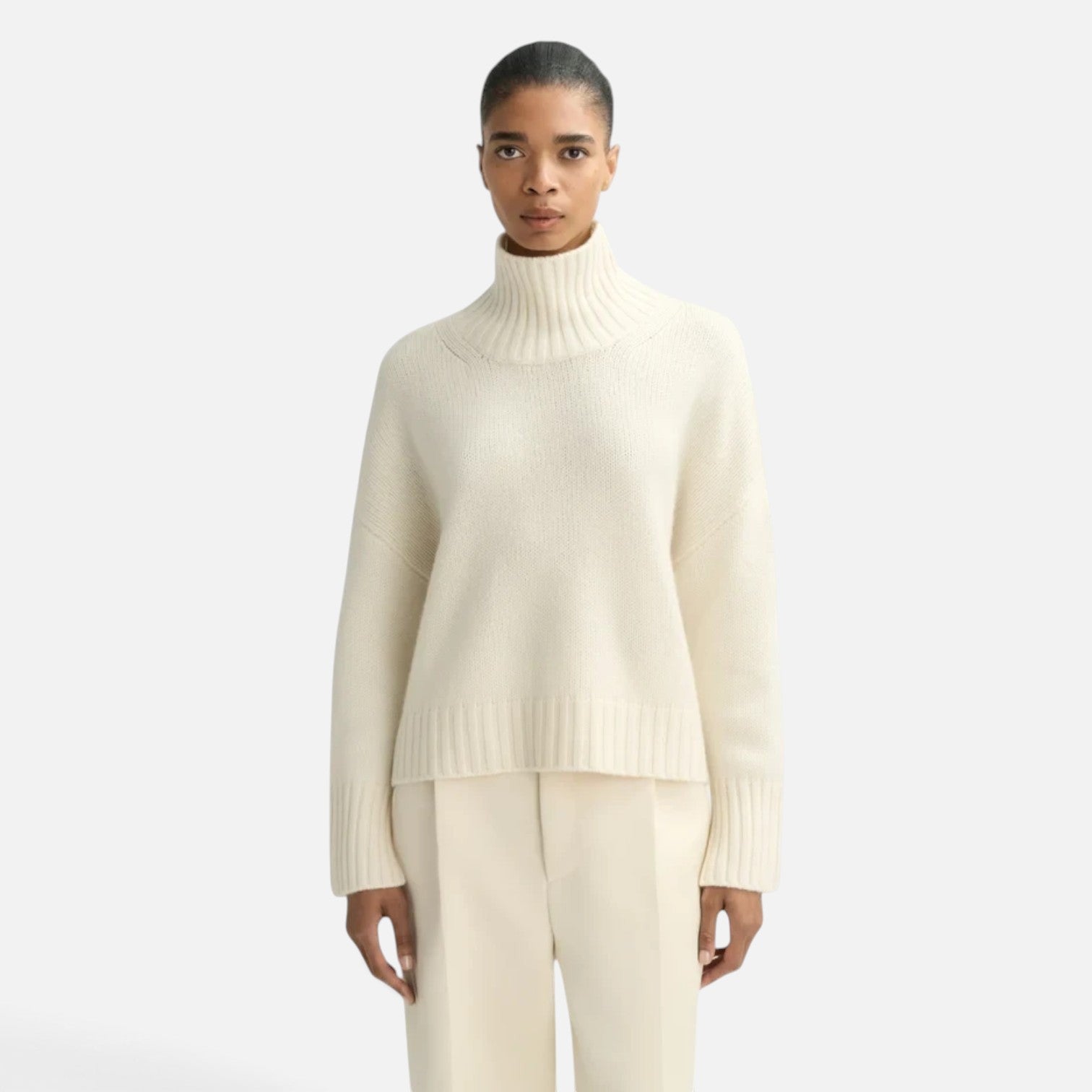 Model wearing a Shop Rescue Spa chunky cream cashmere turtleneck sweater with sleeve slits and a relaxed fit.