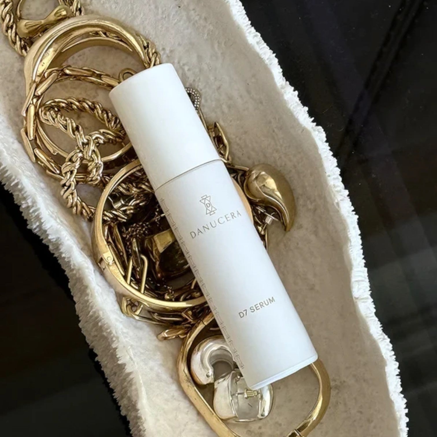 Shop Rescue Spa D7 Serum in a white bottle resting on a textured white dish surrounded by gold jewelry.