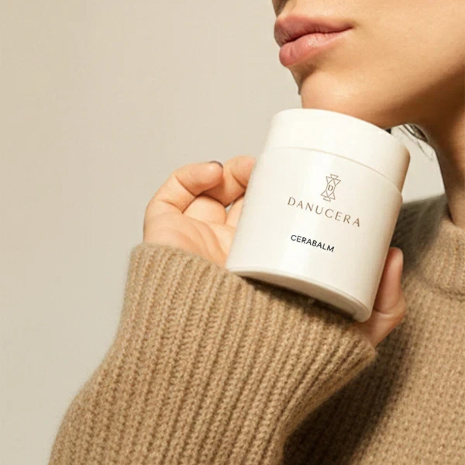 Shop Rescue Spa Danucera Cerabalm multi-purpose cleansing balm held by a model wearing a cozy beige sweater
