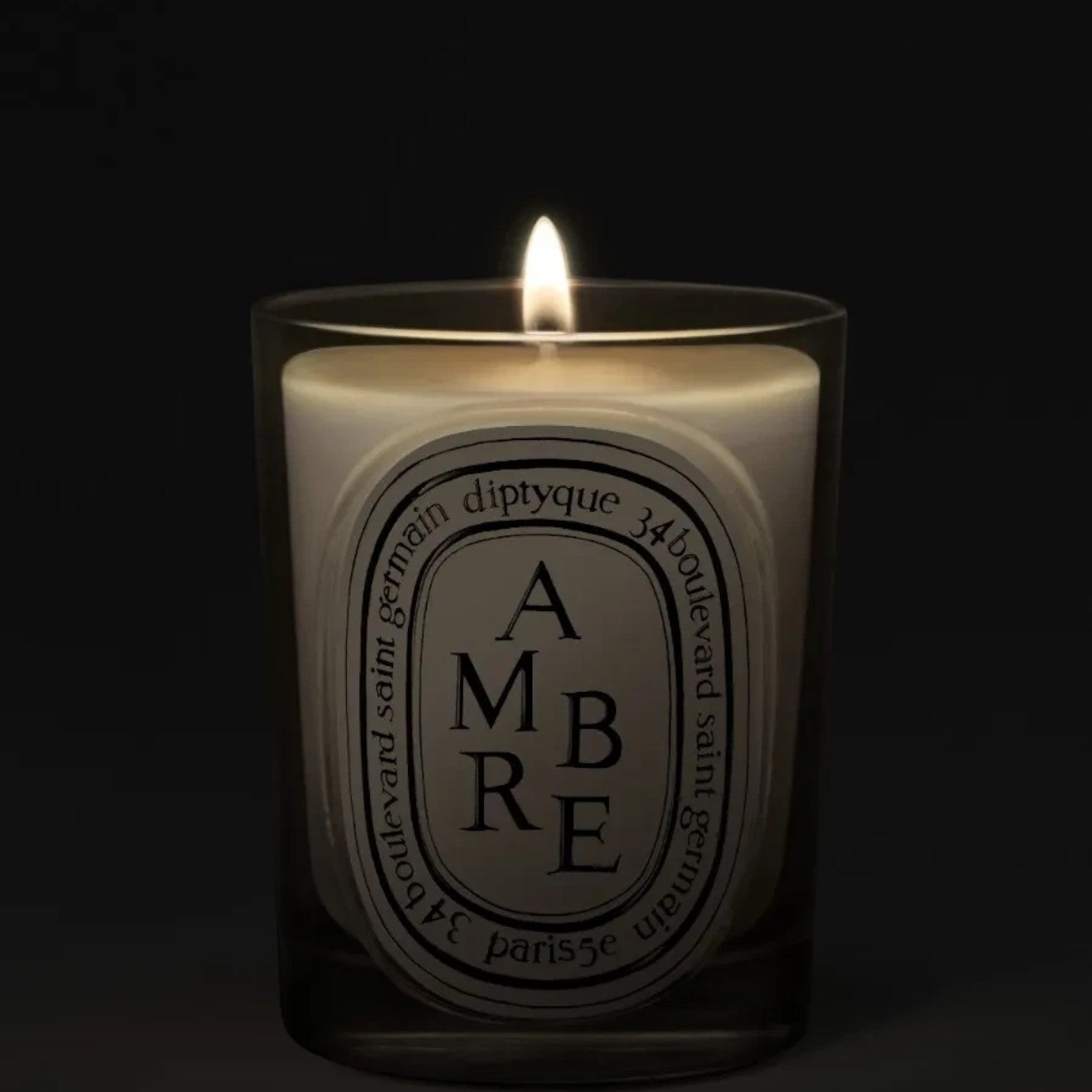 Shop Rescue Spa Diptyque Ambre scented candle in a glass vessel with a glowing flame against a dark background