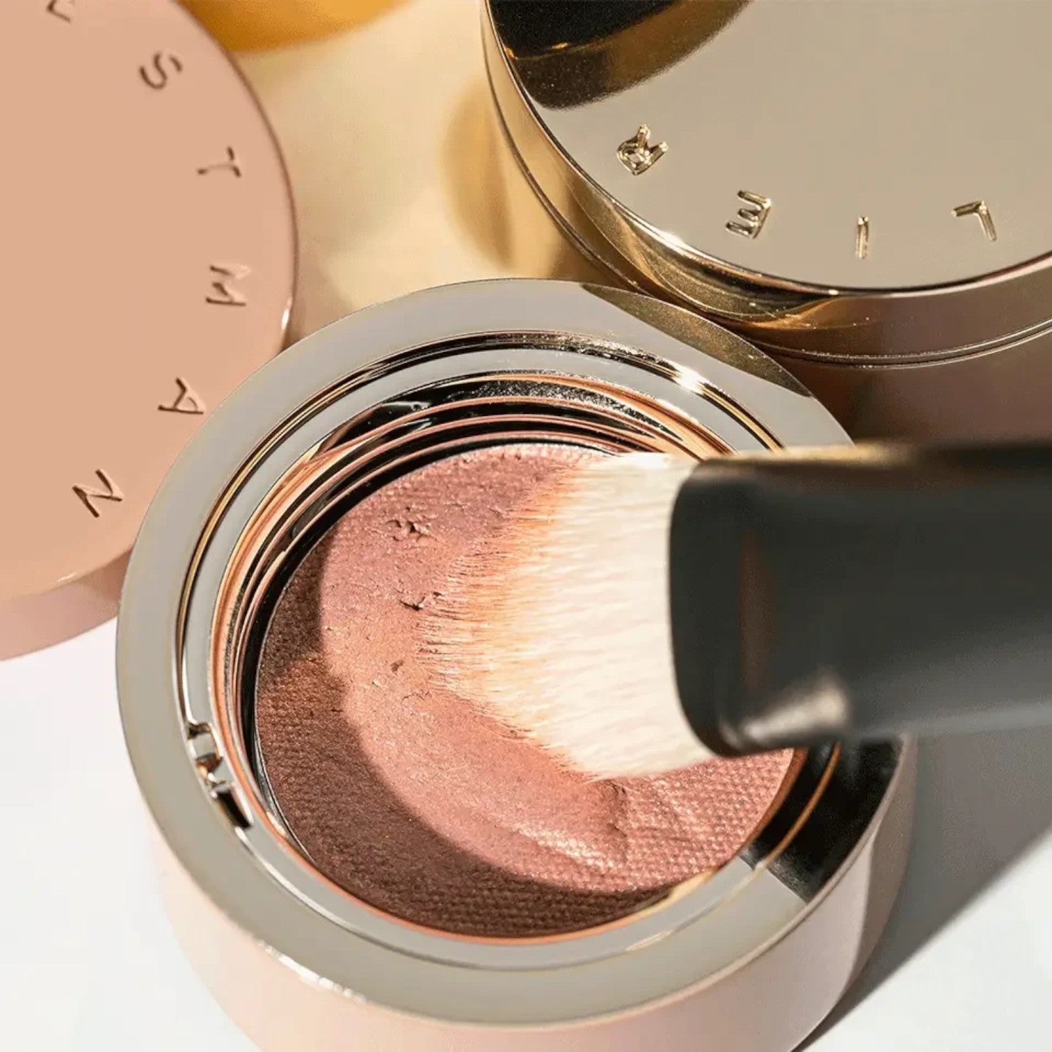 Shop Rescue Spa Eye Shadow Brush I applying soft pink cream shadow from a compact with a metallic gold lid