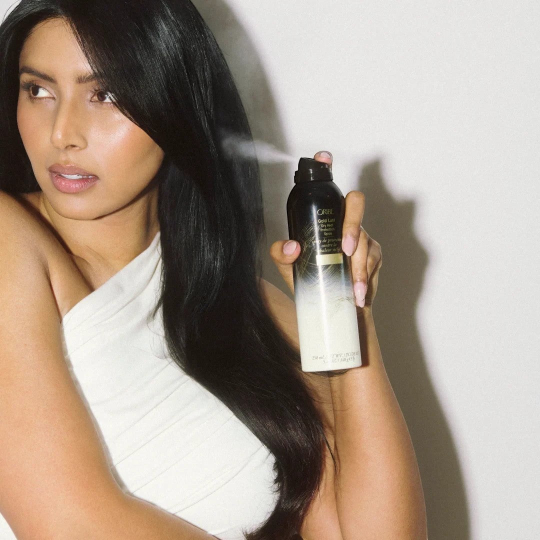 Shop Rescue Spa model with long dark hair spraying Oribe Gold Lust Dry Heat Protection Spray, protecting hair from heat.