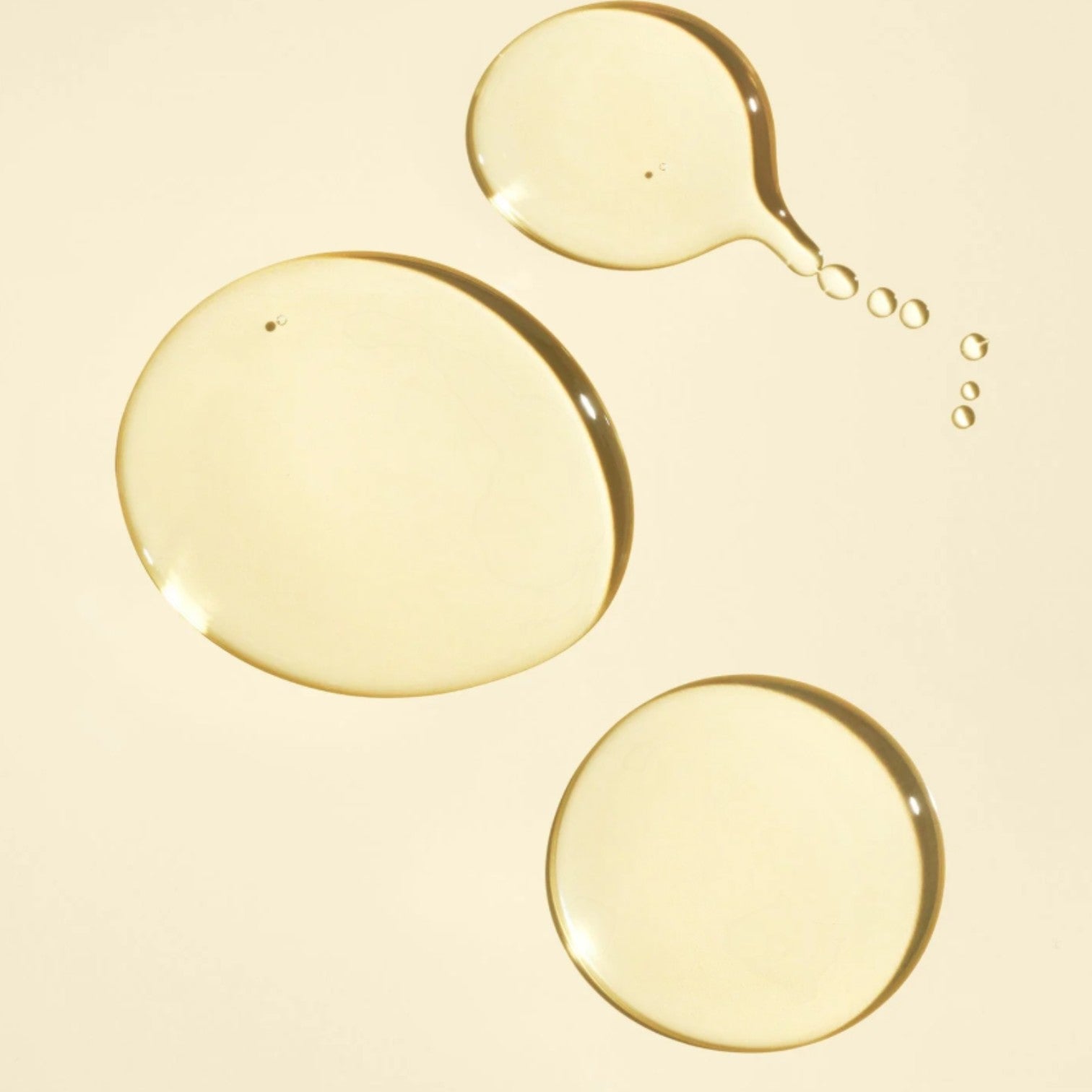 Shop Rescue Spa Gold Lust Nourishing Hair Oil, a golden, viscous liquid with three large drops and several smaller droplets on a pale yellow background.
