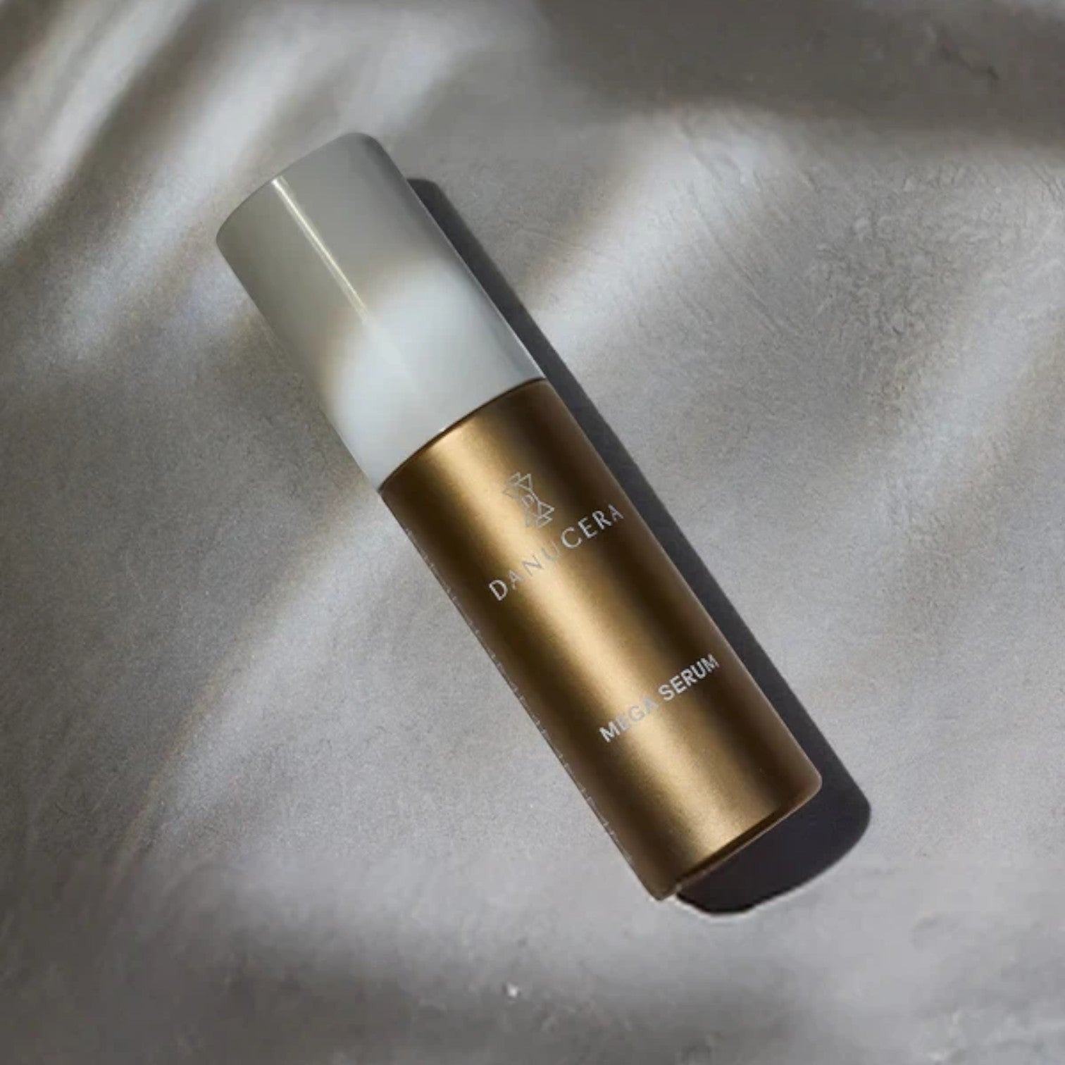 Shop Rescue Spa Danucera Mega Serum in a metallic gold bottle with a white cap, resting on a soft grey fabric.