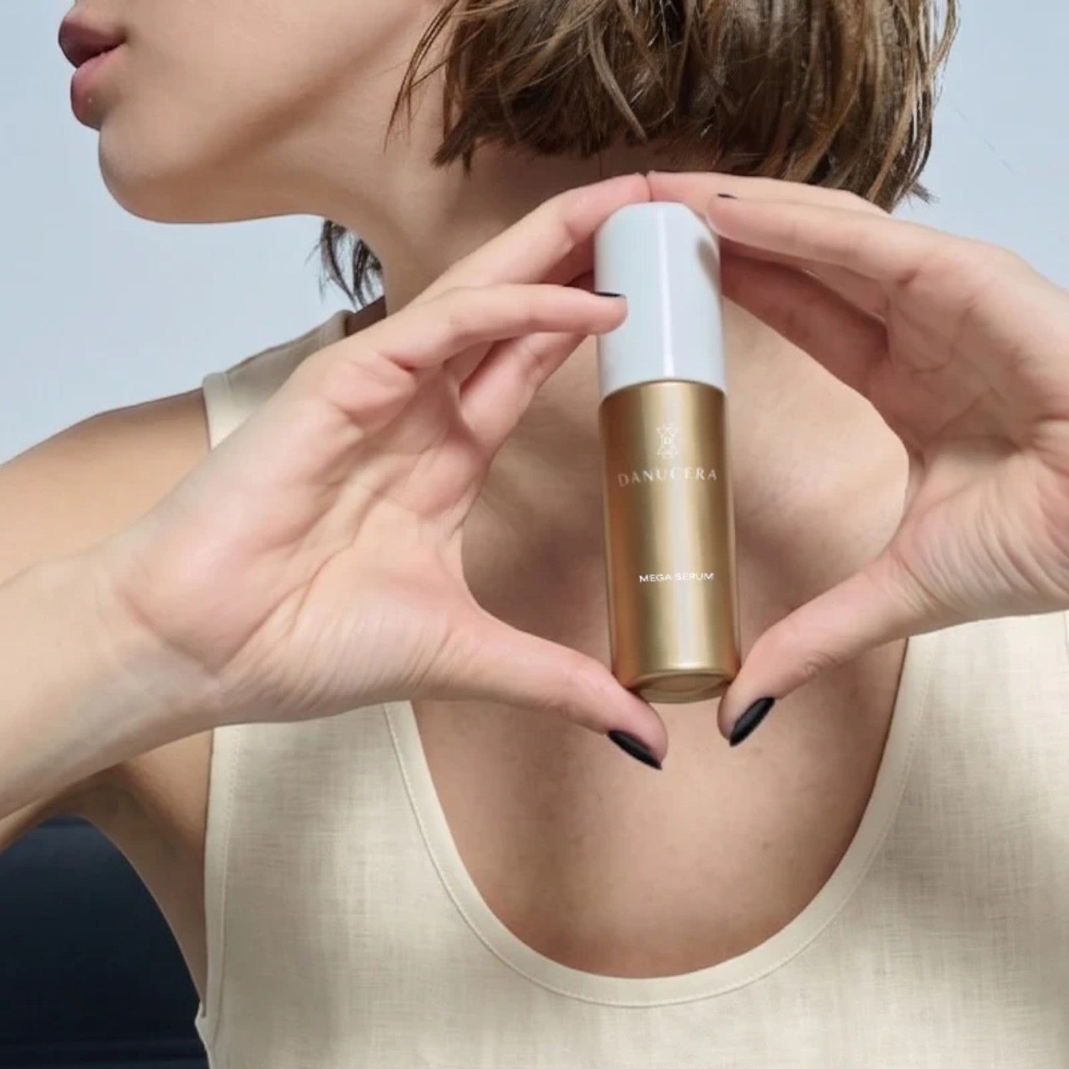 A woman holding a gold Shop Rescue Spa Mega Serum bottle with a white cap, featuring a minimalist, elegant design.