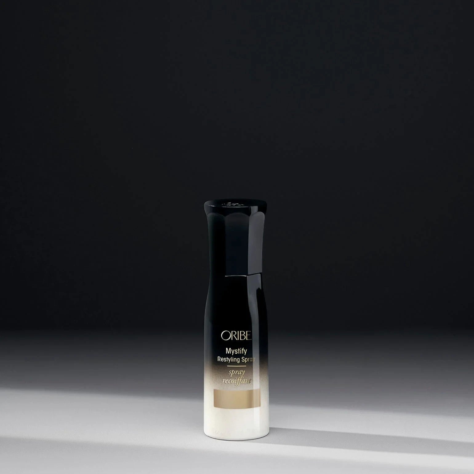 Oribe Mystify Restyling Spray bottle with gold and white gradient, provides heat protection and strengthens hair.