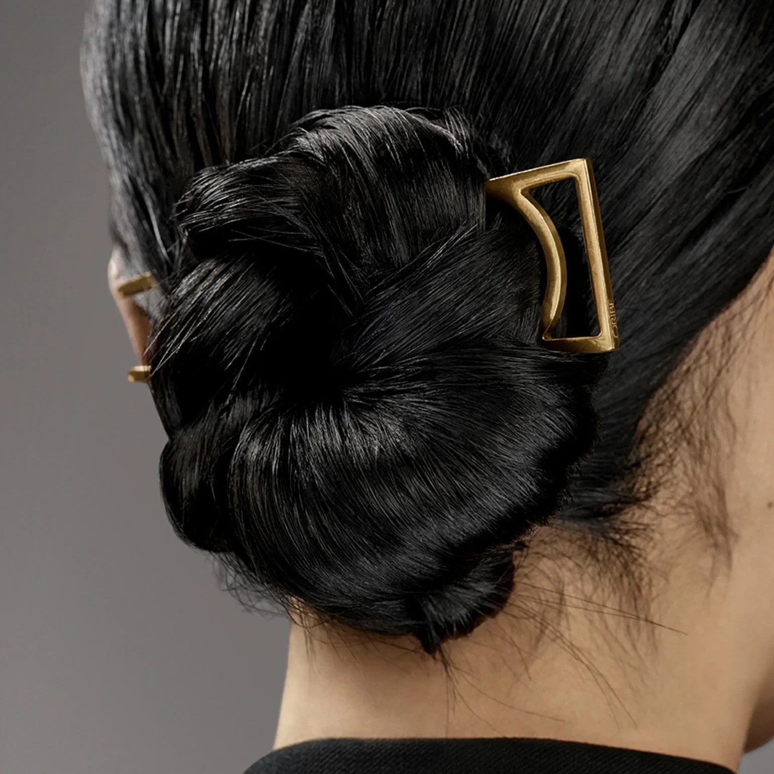 Shop Rescue Spa Oribe Superfine Hair Spray used on a sleek, shiny black hair bun secured with a gold geometric clip.