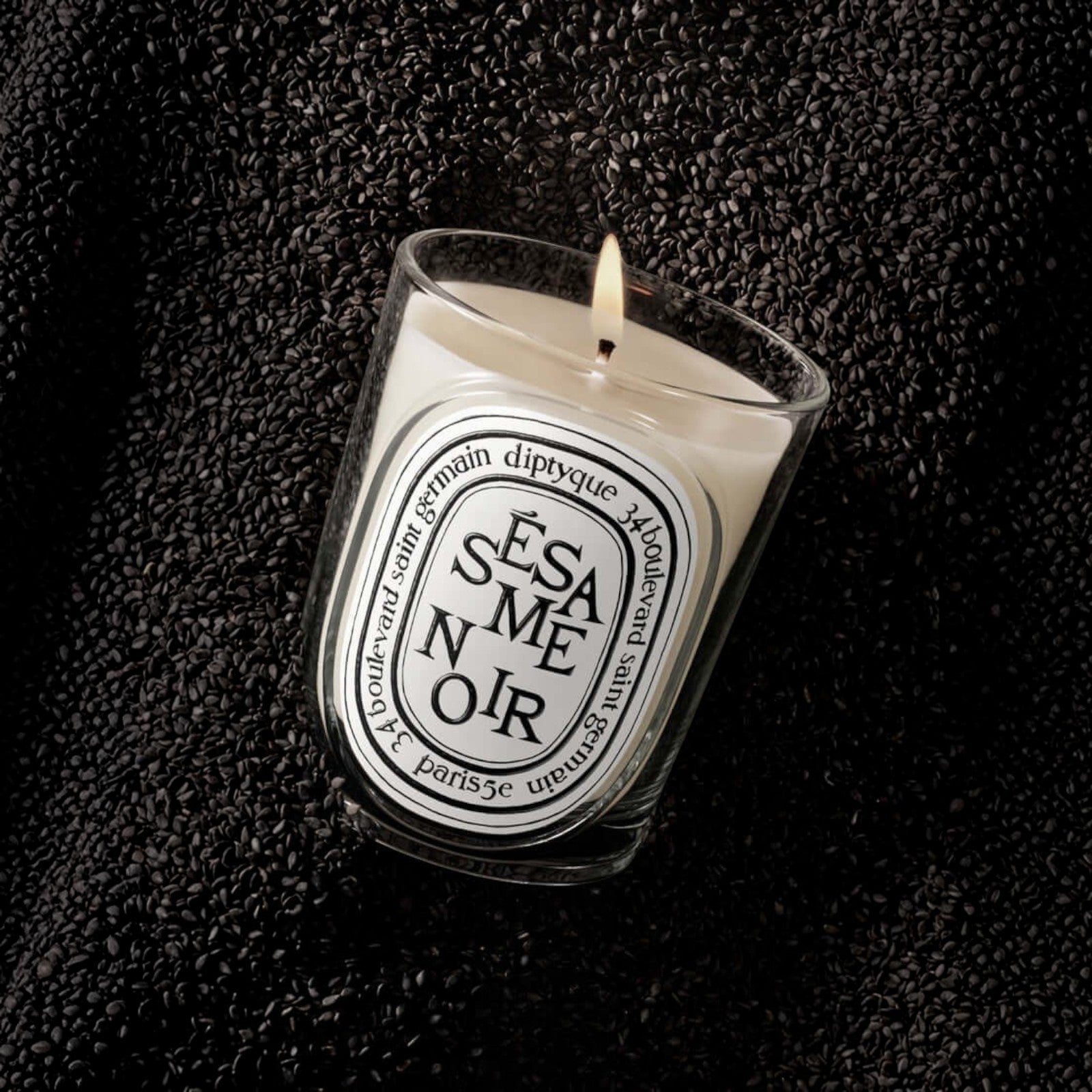 Shop Rescue Spa Sesame Noir scented candle in a glass vessel, surrounded by a bed of roasted black sesame seeds.
