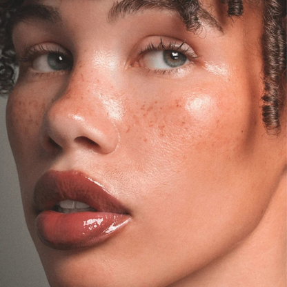 Shop Rescue Spa ÂN-GLOSS Ceramide Lip Tint on a model with freckles, showing a shimmery pink high-shine finish.
