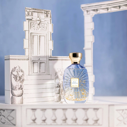 Shop Rescue Spa Blue Madeleine fragrance bottle with gold flakes inside, set against a whimsical paper illustration.