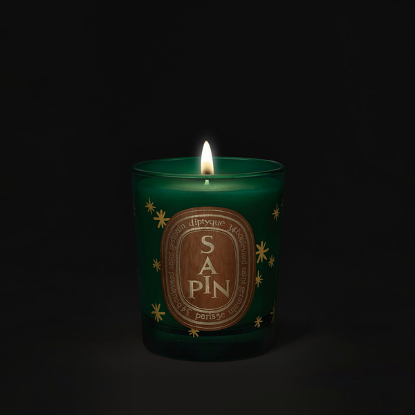Shop Rescue Spa Diptyque Sapin holiday candle in a green glass jar with gold star accents and a glowing flame.