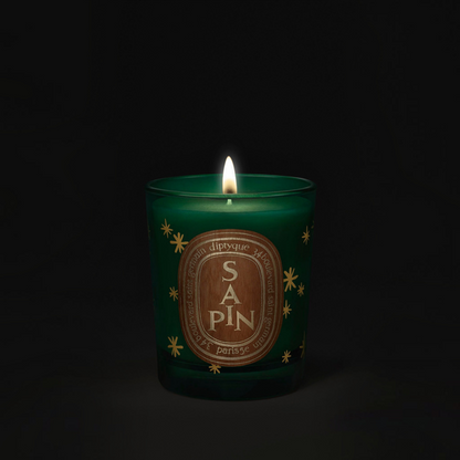 Shop Rescue Spa Diptyque Sapin holiday candle in a green glass jar with gold star accents and a glowing flame.