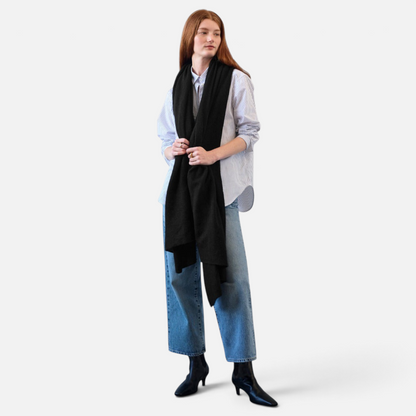 Shop Rescue Spa black cashmere travel wrap worn by a woman over a striped shirt and blue jeans