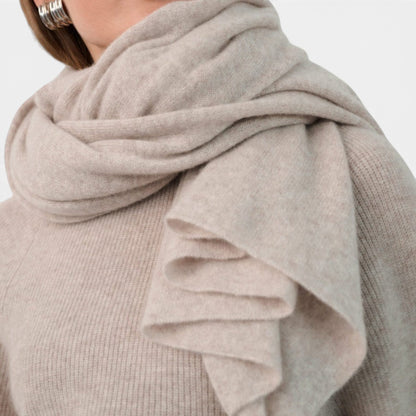 Shop Rescue Spa beige cashmere travel wrap worn as a cozy, oversized scarf over a matching knit sweater.