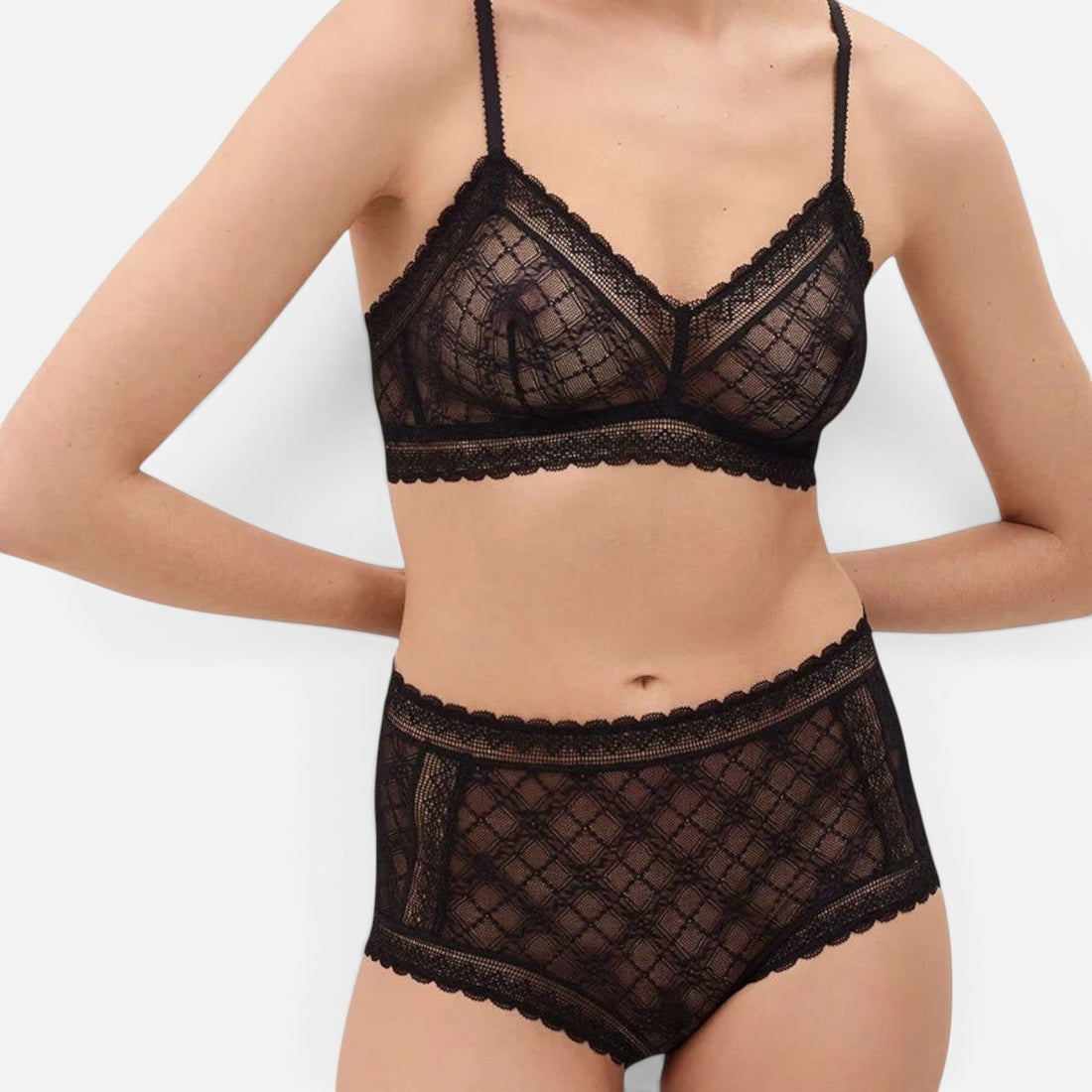 A model wearing a black lace bralette and matching high-waisted briefs against a light gray studio background.