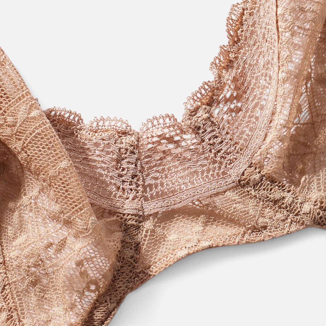 Close-up of a lace bra in a warm champagne beige color, showing intricate floral embroidery and scalloped edges against a light gray background.