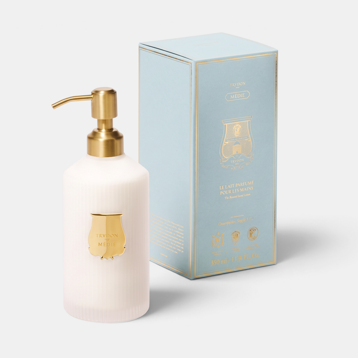 Shop Rescue Spa Trudon Médie scented hand lotion in a white ribbed bottle with a gold pump next to its blue box.