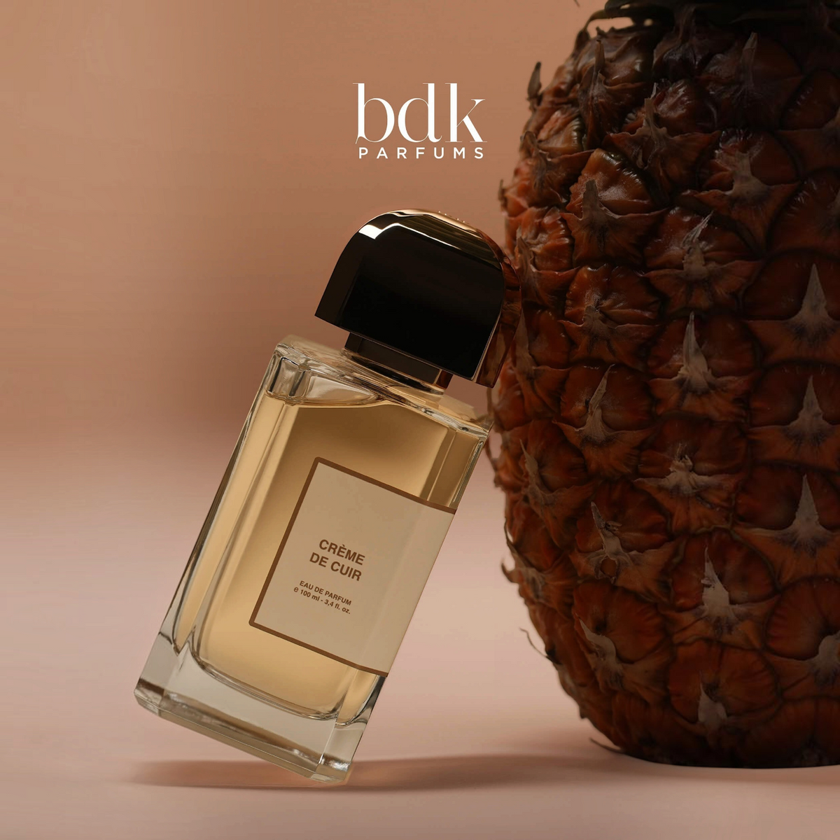Shop Rescue Spa BDK Parfums Creme De Cuir 100ml perfume bottle next to a fresh pineapple on a beige background