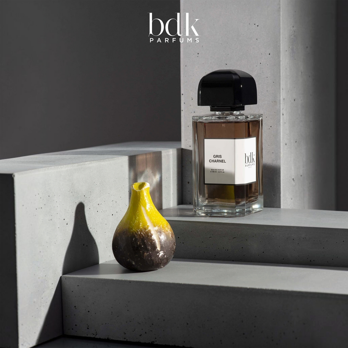 Shop Rescue Spa BDK Parfums Gris Charnel 100ml perfume bottle on a grey concrete display with a decorative fig object