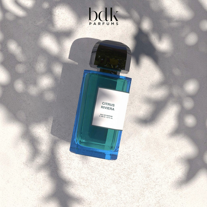Shop Rescue Spa Citrus Riviera eau de parfum in a rectangular blue glass bottle with a black cap on a textured surface