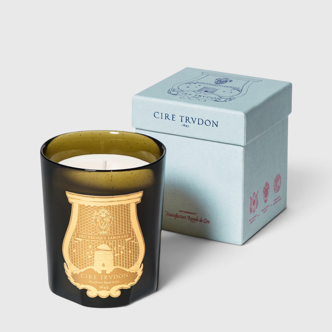 Shop Rescue Spa Ottoman Classic Candle in a dark green glass vessel with a gold emblem next to its light blue box.