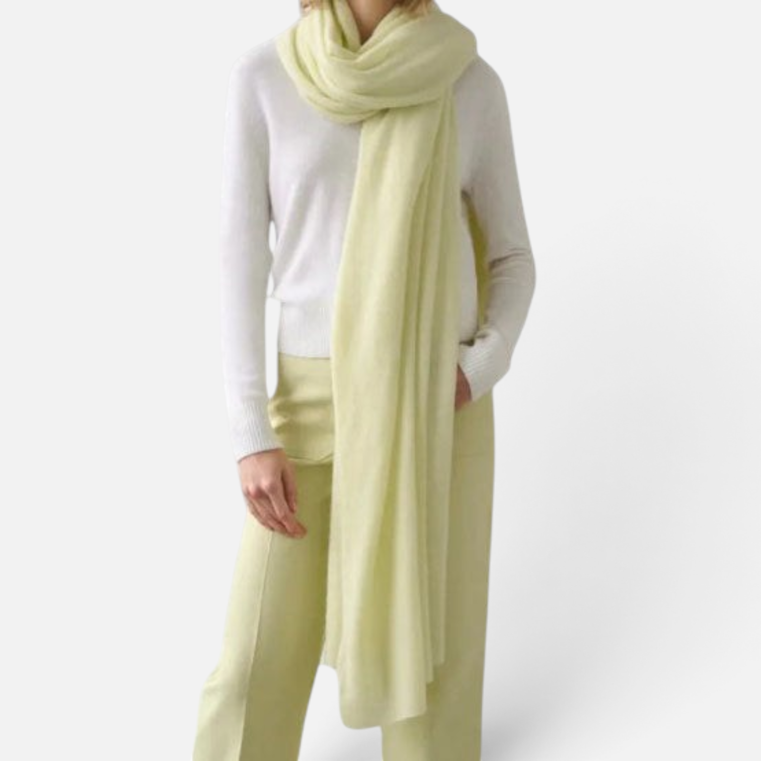 Shop Rescue Spa pale yellow cashmere travel wrap draped over a model wearing a white sweater and matching trousers.