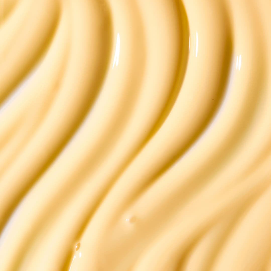 A close-up texture shot of a thick, creamy pale yellow cosmetic or food product with smooth, wavy ridges.