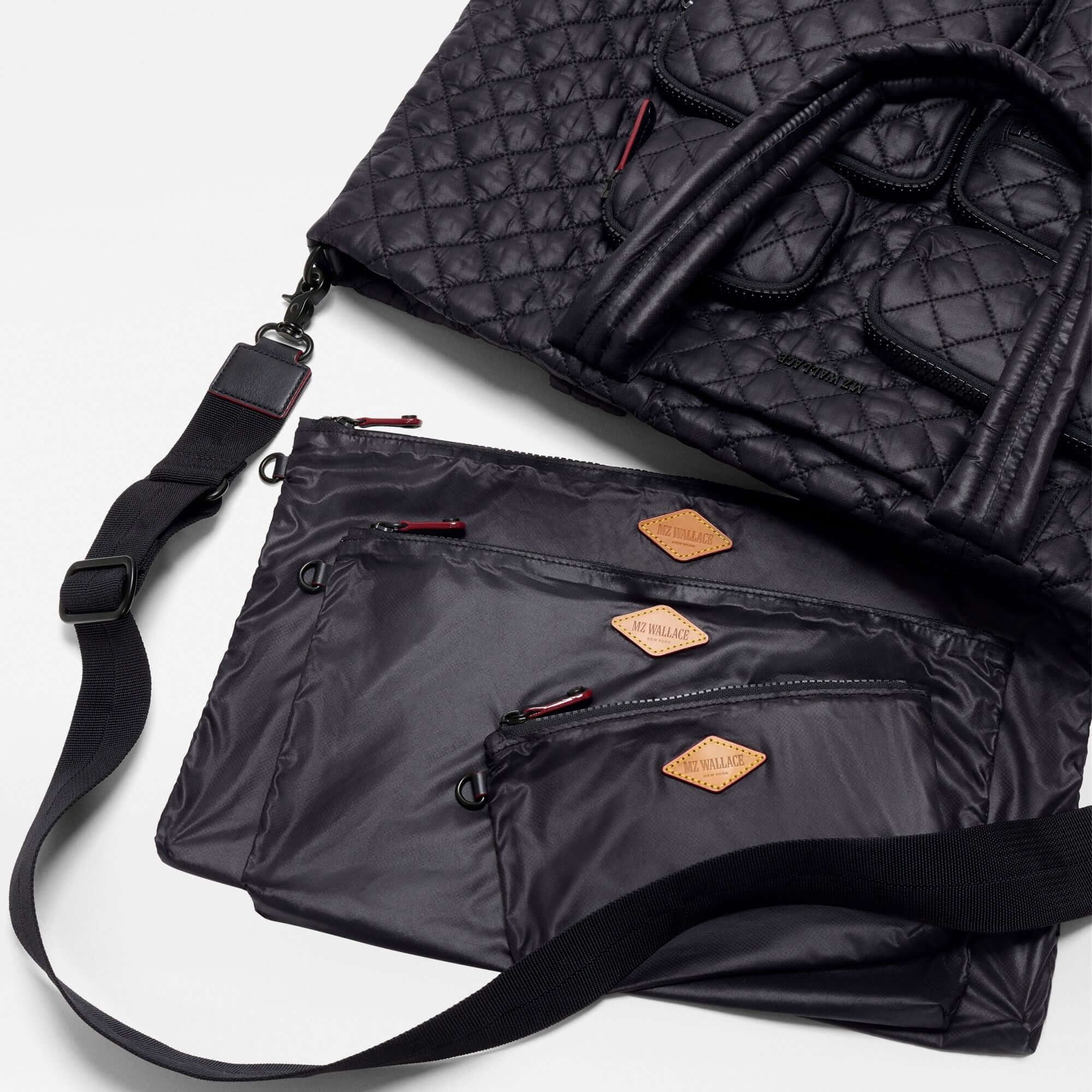 A black quilted puffer bag with a matching zippered pouch and shoulder strap, laid out on a white background. The bags feature small tan diamond-shaped leather patches on the pouch.