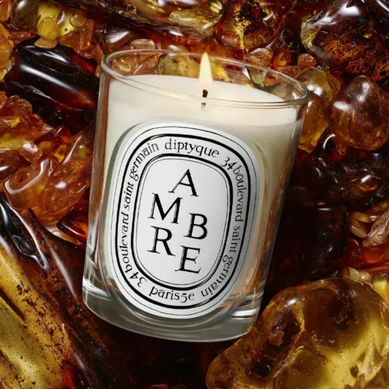 Shop Rescue Spa Diptyque Ambre scented candle in a glass vessel surrounded by glowing amber resin fragments