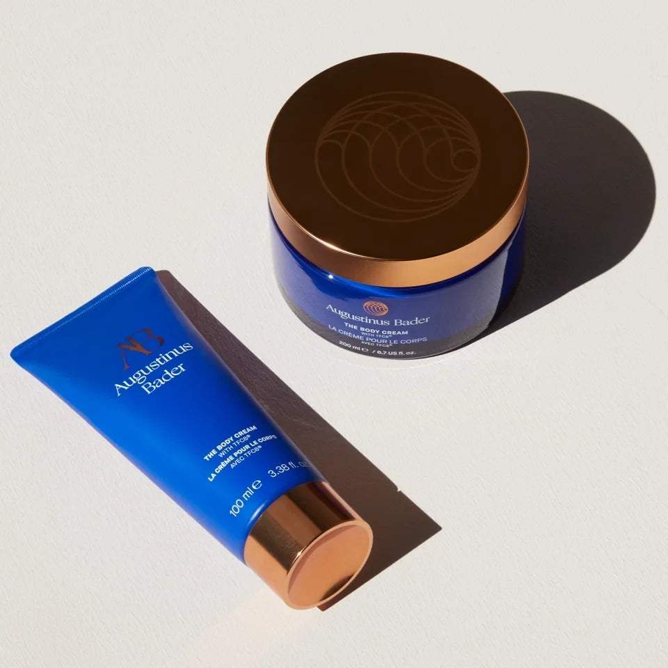 Shop Rescue Spa Augustinus Bader The Body Cream in a blue jar and tube with metallic bronze lids on a white surface