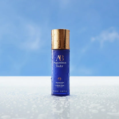 Shop Rescue Spa Augustinus Bader The Face Mist in a blue bottle with a gold cap, covered in refreshing water droplets.