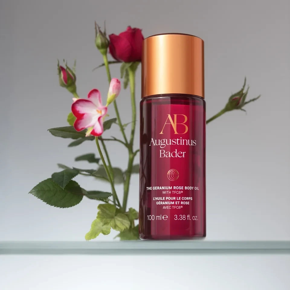 Shop Rescue Spa Augustinus Bader The Geranium Rose Body Oil in a red glass bottle with a rose flower background