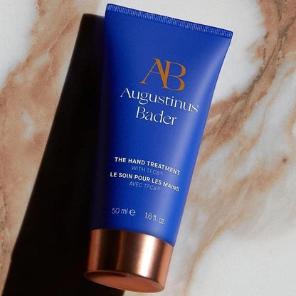 Shop Rescue Spa Augustinus Bader The Hand Treatment in a blue 50ml tube with a metallic copper cap on marble surface