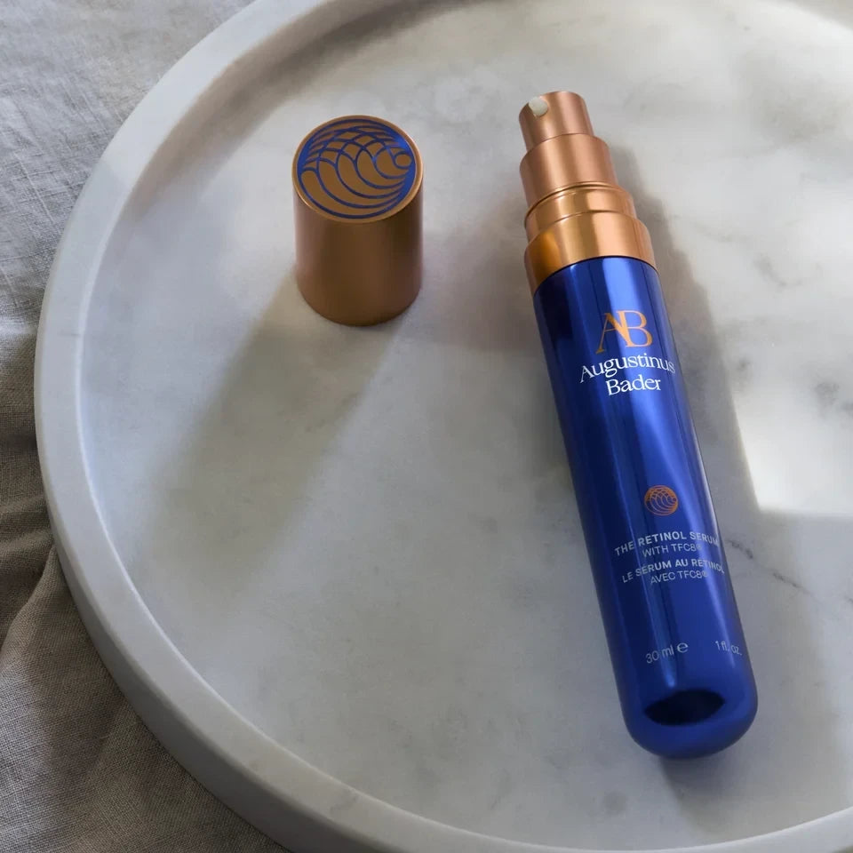 Shop Rescue Spa Augustinus Bader The Retinol Serum in a blue pump bottle with a gold cap on a white marble tray