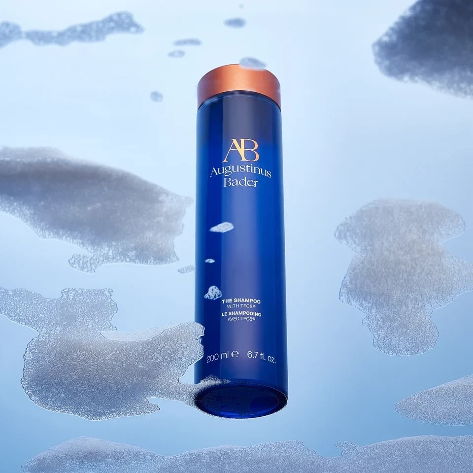 Shop Rescue Spa Augustinus Bader The Shampoo in a blue bottle surrounded by white foam on a light blue background