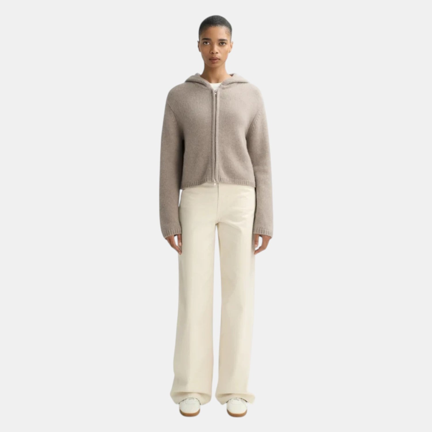 Shop Rescue Spa chunky knit cashmere hoodie in beige with a front zipper, worn by a model with cream trousers.