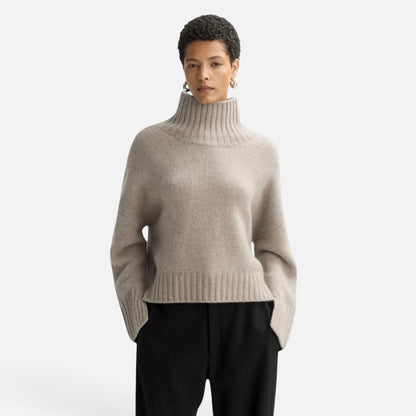 Model wearing a Shop Rescue Spa beige chunky cashmere turtleneck sweater with sleeve slits and a relaxed fit.