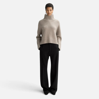 Model wearing a Shop Rescue Spa beige chunky cashmere turtleneck sweater with sleeve slits and a relaxed fit.