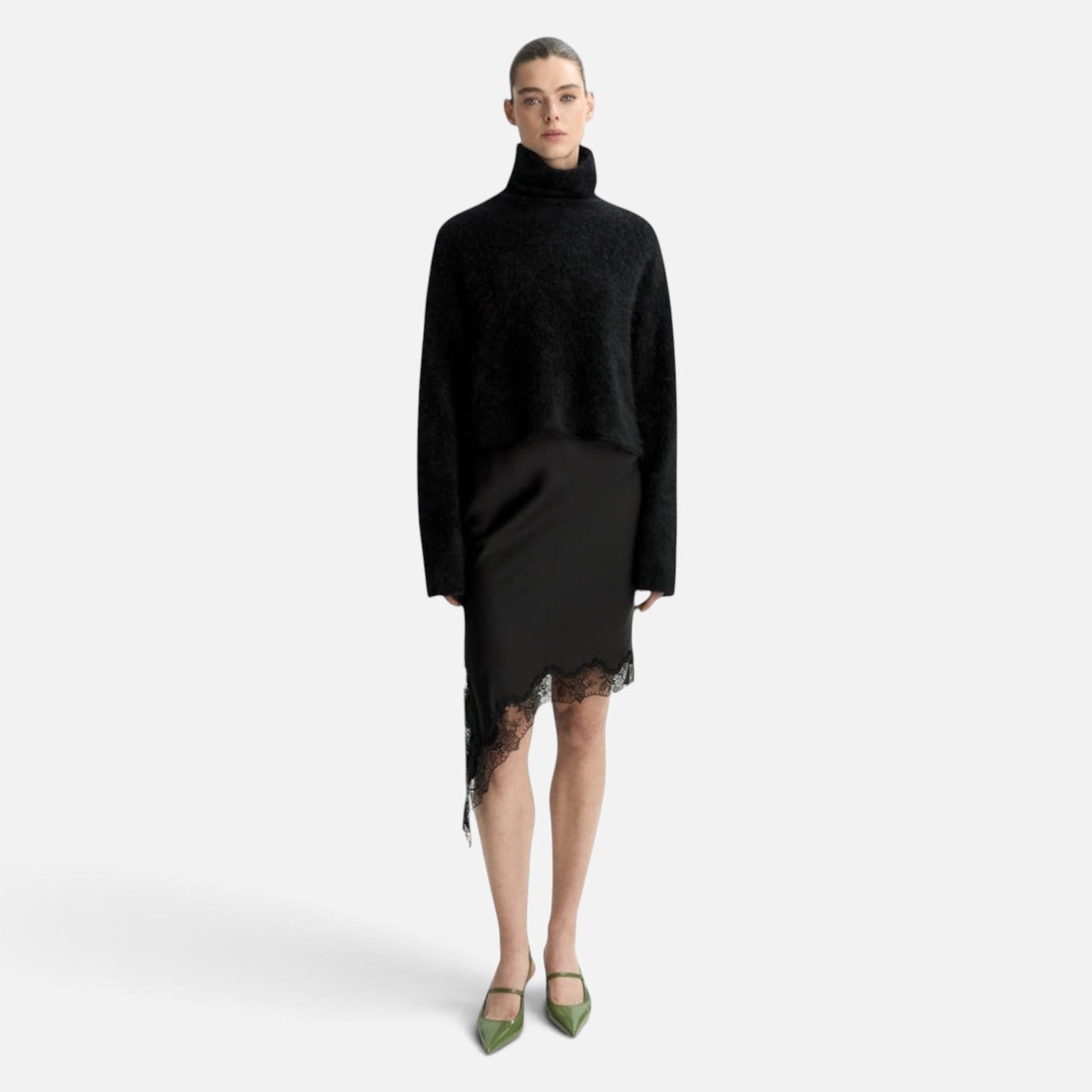 Model wearing a Shop Rescue Spa black chunky cashmere turtleneck sweater with sleeve slits and a lace-trim skirt.