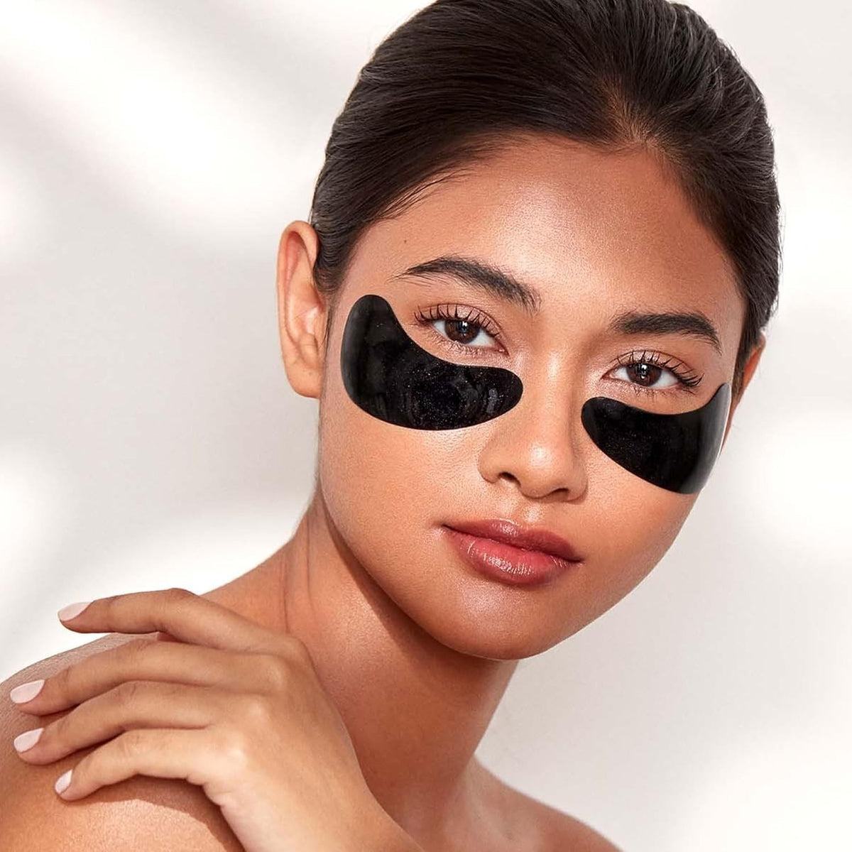 Shop Rescue Spa Celestial Black Diamond hydrogel eye masks applied under the eyes of a woman for a refreshed look.