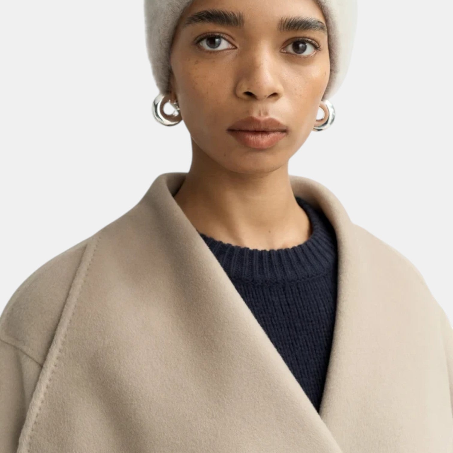Shop Rescue Spa brushed cashmere beanie in a soft beige tone worn by a model with silver hoop earrings.