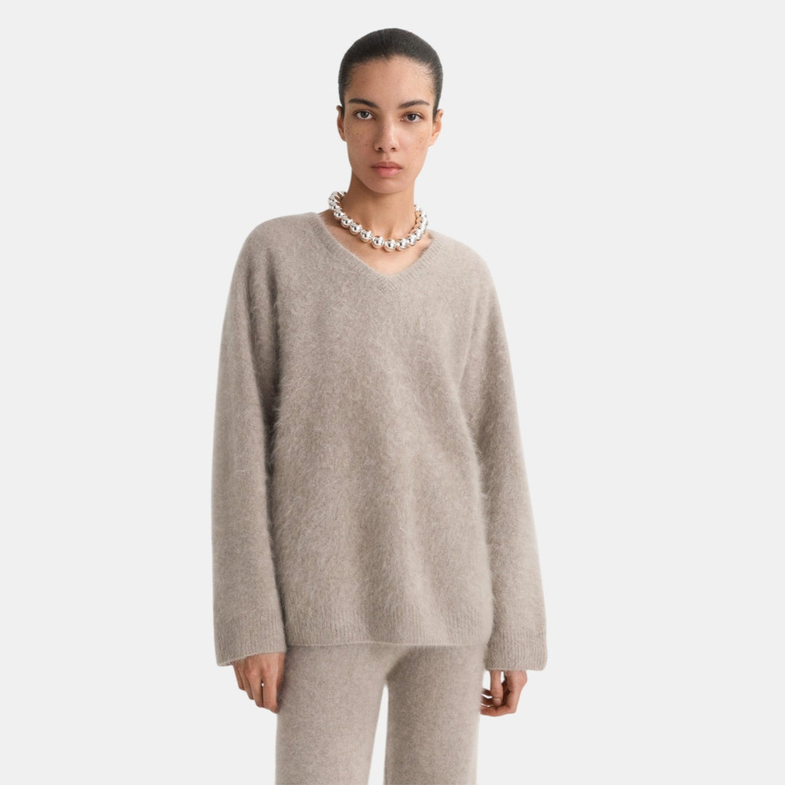 Shop Rescue Spa brushed cashmere V-neck sweater in beige worn by a model with a chunky silver necklace