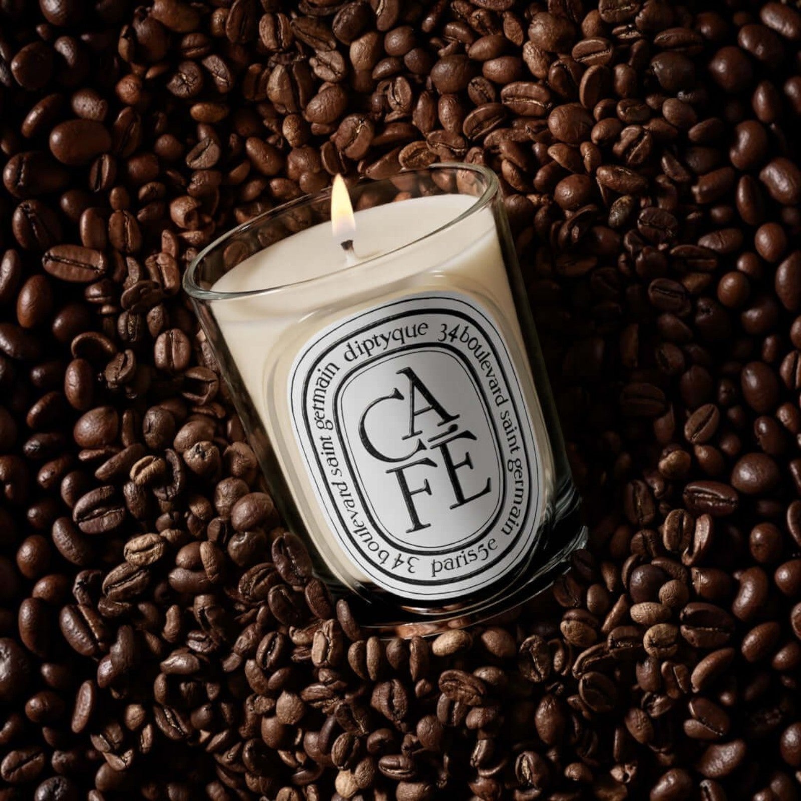 Shop Rescue Spa Cafe scented candle in a glass vessel, surrounded by roasted coffee beans with a warm glowing flame.